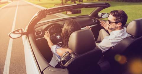 Man en een vrouw in een cabrio aan het rijden op een weg